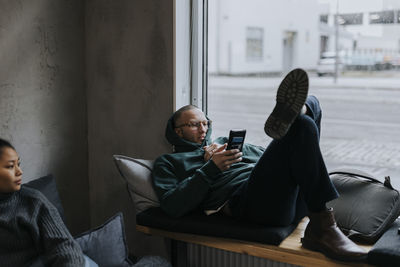 Young businessman using smart on seat by female colleague at creative office