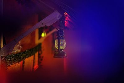 Illuminated lighting equipment hanging by building against sky at night