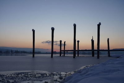 Wooden posts on snow covered land against sky during sunset