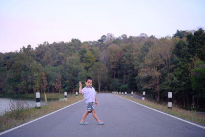 Portrait of boy gesturing peace sign while standing on road