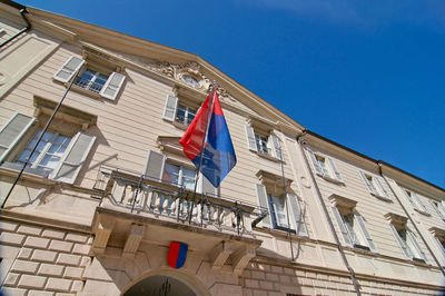 Low angle view of flags on building against clear blue sky