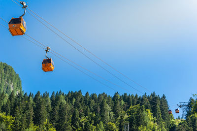 Low angle view of overhead cable cars in forest against clear sky