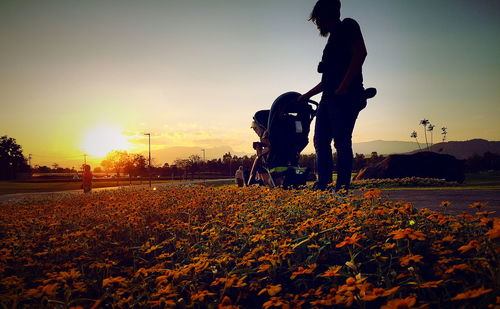 Low angle view of man standing by baby carriage at park during sunset