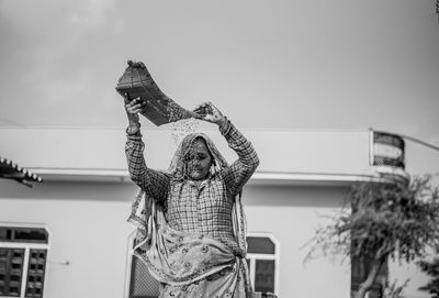 Low angle view of woman standing by building against sky