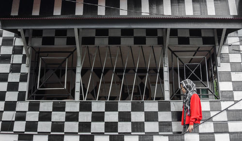 Rear view of woman with umbrella against building