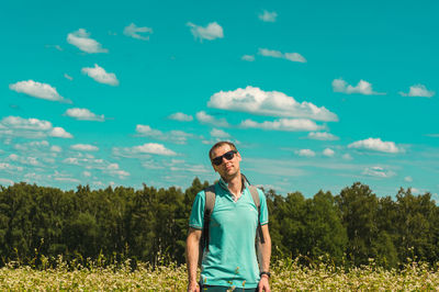 Portrait of young man standing on field against sky