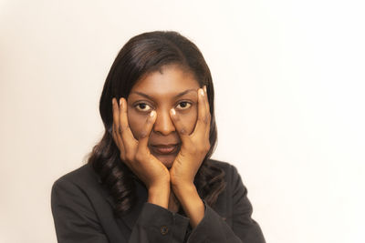Portrait of young woman with hands on face standing against beige background
