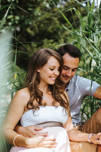 Husband sitting with pregnant wife against plants