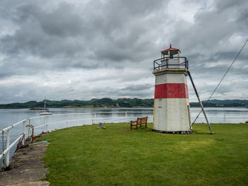 Lighthouse by calm sea against cloudy sky