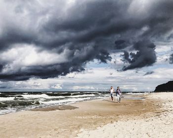People standing on beach against cloudy sky