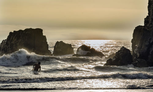 Man standing on cliff by sea against sky