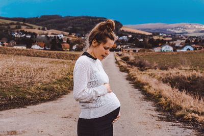 Pregnant woman standing on road amidst field