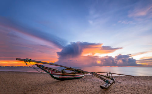 Boat moored on beach against sky during sunset