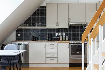 Interior of contemporary kitchen with white furniture and black tile on wall designed in minimal style in house