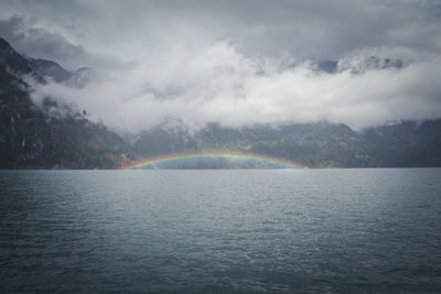 Scenic view of rainbow over sea and mountains against sky
