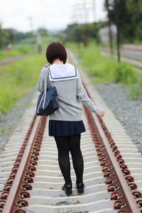 Rear view of woman in school uniform on railroad track