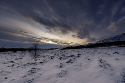 Snow covered landscape against sky during sunset