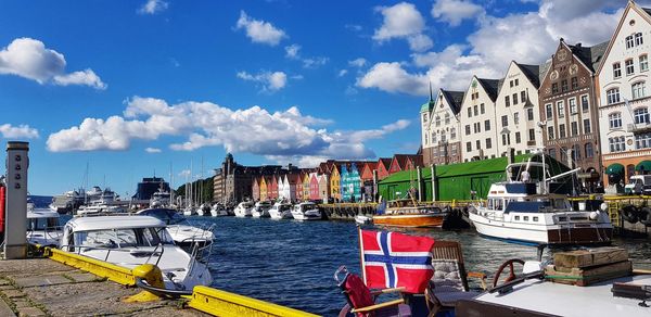 Sailboats moored on canal amidst buildings in city against sky