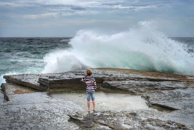 Rear view of boy standing against sea waves