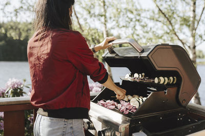 Young woman preparing food on barbecue grill during dinner party