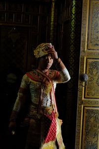 Woman holding camera while standing against wall