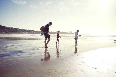 Full length of father with children walking at beach on sunny day