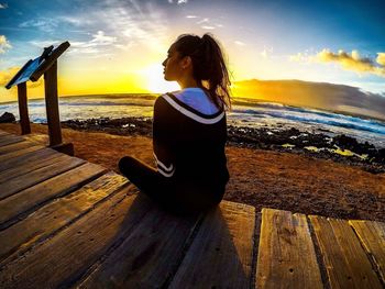 Woman sitting on beach against sky during sunset