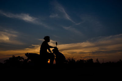 Silhouette man on motor scooter against sky during sunset
