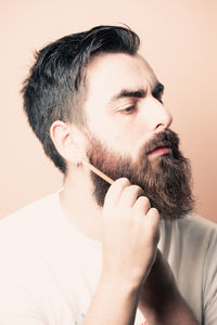 Close-up of young man smoking cigarette against pink background