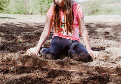 Low section of girl kneeling on soil at farm