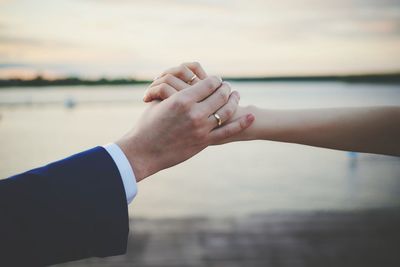Close-up of couple holding hands against sea
