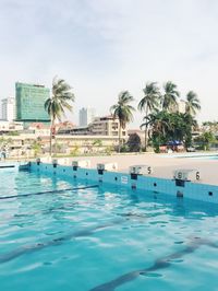 Swimming pool by coconut palm trees in city against sky