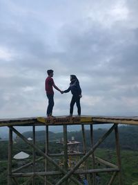 Young couple holding hands at built structure against sky