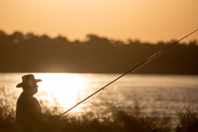 Silhouette man fishing against sky during sunset