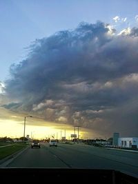 Cars on road against cloudy sky at sunset