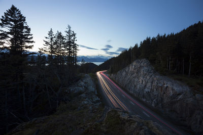 Light trails on road by mountain against sky