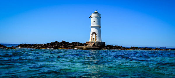 Lighthouse by sea against clear sky