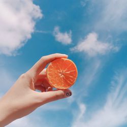 Cropped hand of woman holding orange slice against sky