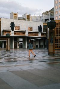 Rear view of man walking on wet road in city during rainy season