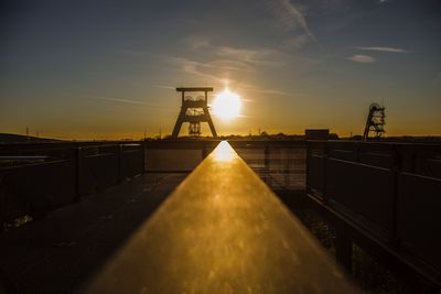 Bridge over factory against sky during sunset