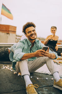 Cheerful young man text messaging on smart phone while enjoying party on terrace