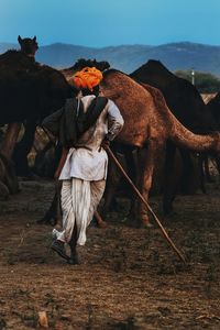 Man with camel standing on field against sky