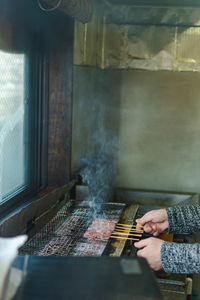 Cropped hands preparing meat on barbecue grill