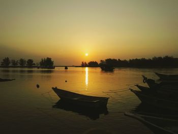 Boats moored in calm lake against romantic sky at sunset