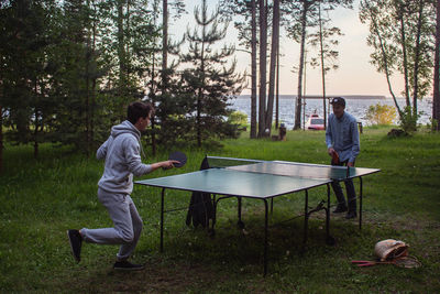 Men playing table tennis on grassy field during sunset