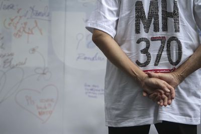 Rear view of man standing with hands behind back against whiteboard