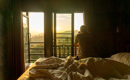 Asian male tourist sits in bed and takes pictures of tea plantations in the morning, chiang rai.