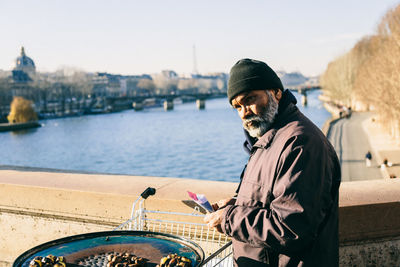 Man standing by river in city against sky