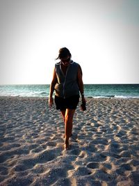 Rear view of young woman walking on beach against clear sky