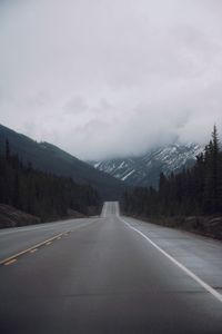 Road leading towards mountain against cloudy sky